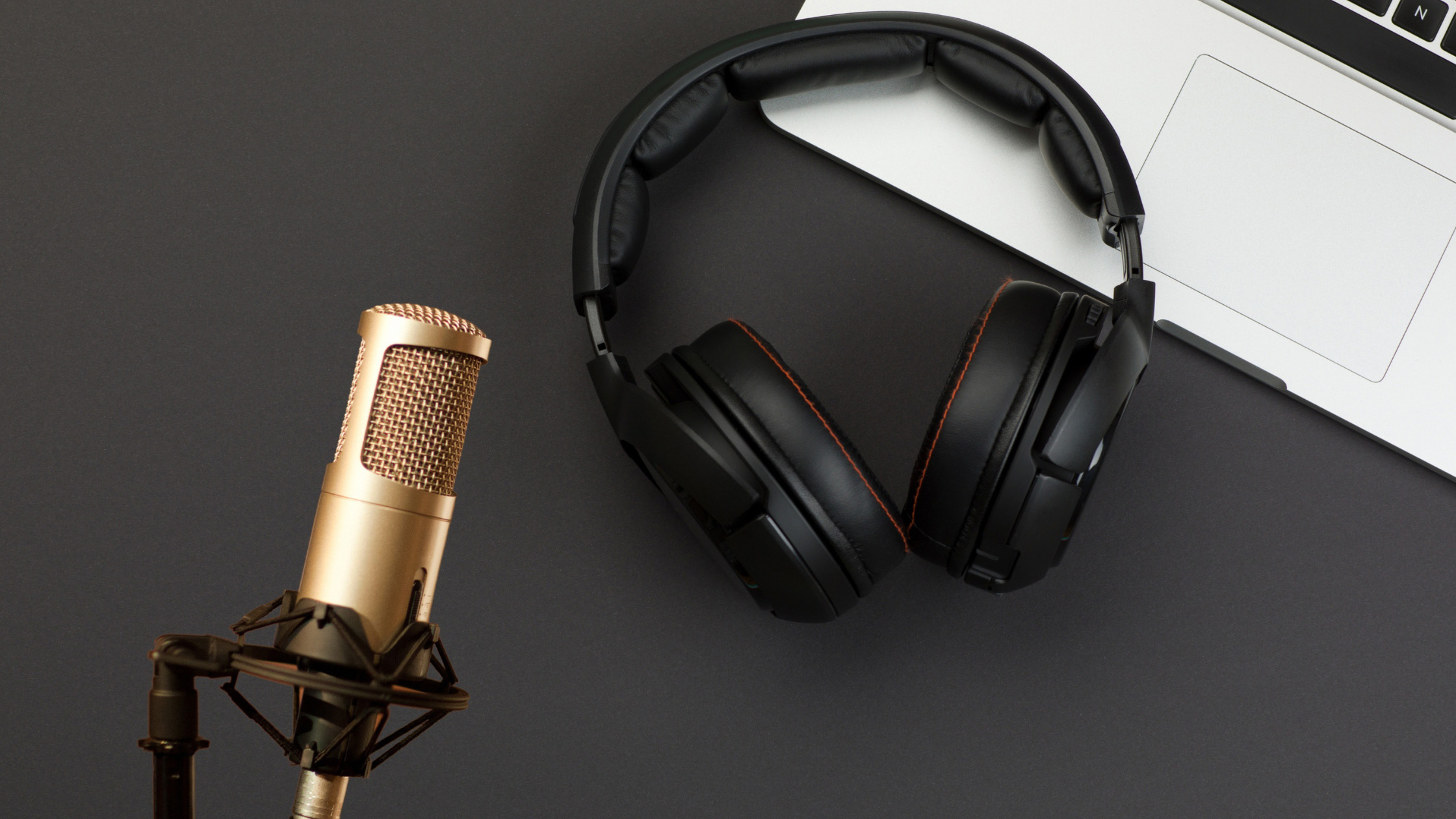Pictured here is a golden microphone, black headphones, and the edge of the silver laptop keyboard.