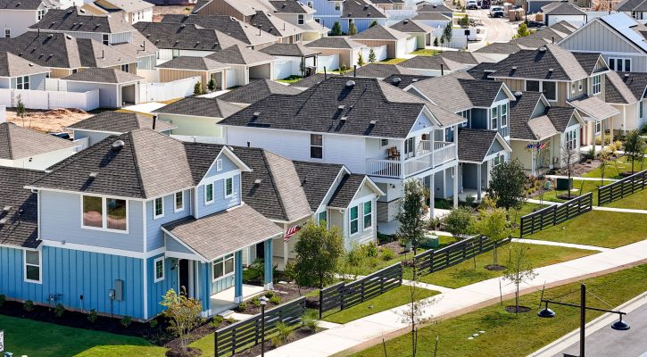 A Street view of two-story and one-story next to fence and sidewalk.
